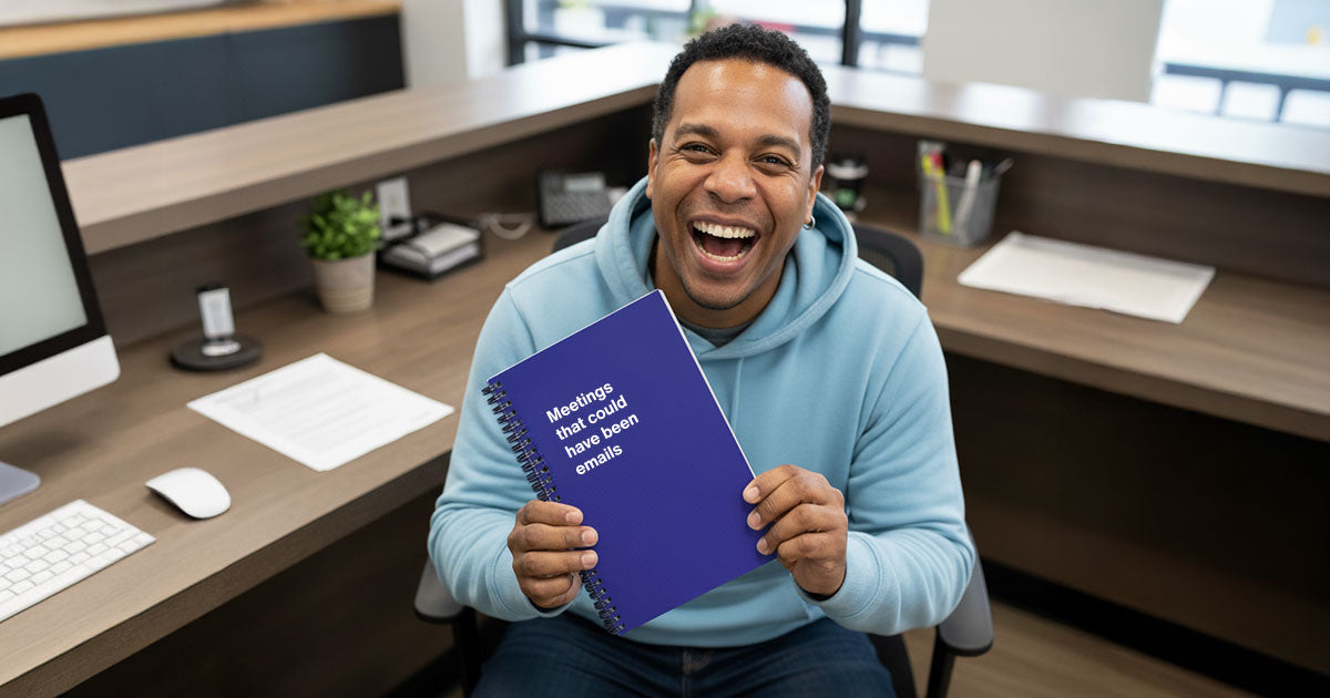 An office worker laughing while holding up his funny WTF Notebook co-worker gift.